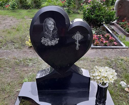 Ein schwarzes, herzförmiges Grabmal mit einem Bild einer Frau darauf, das Trauer und Erinnerung symbolisiert